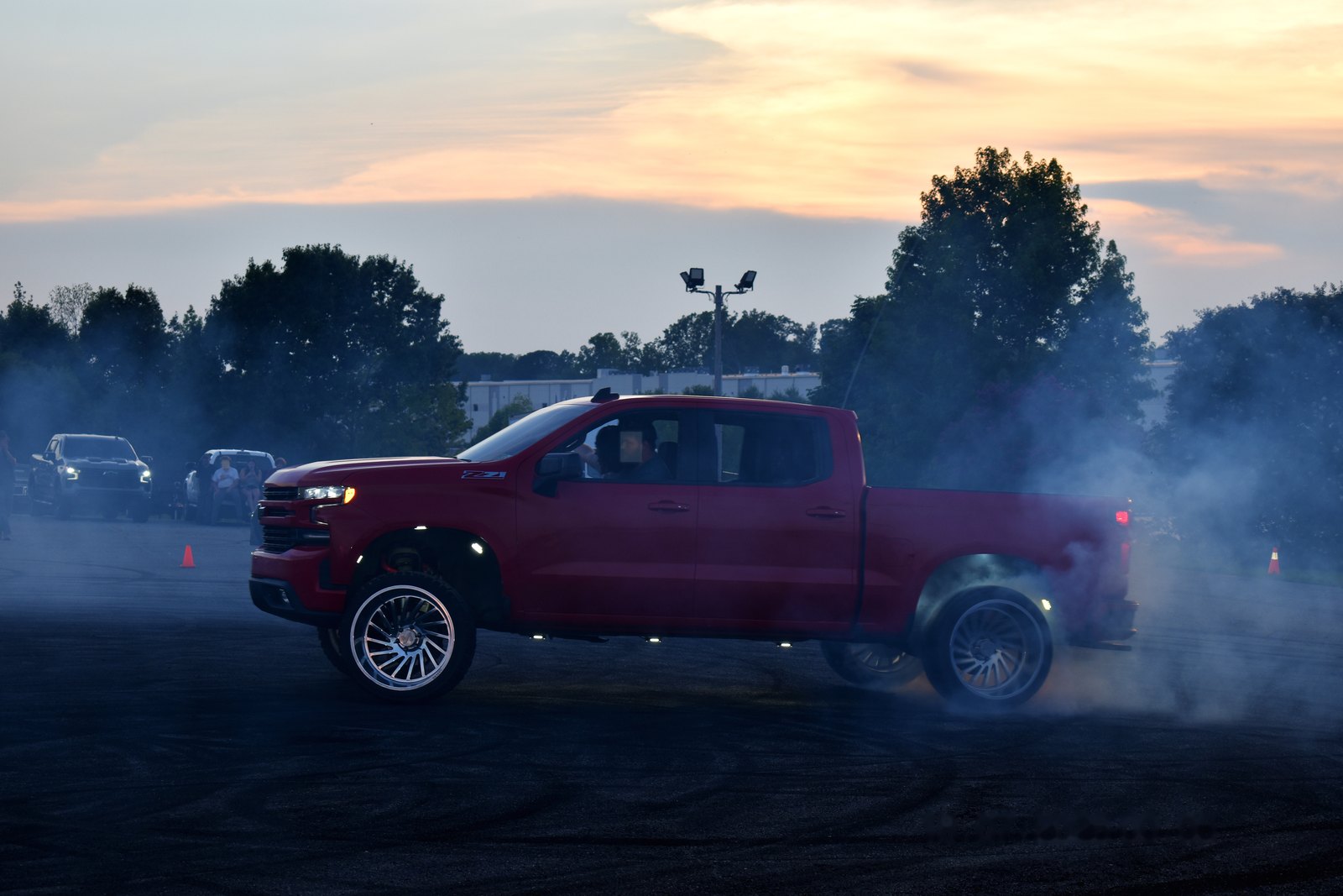 Maroon lifted truck laying down a burnout in tire smoke at dusk during the Eats on 601 truck meet